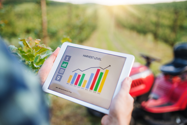 A midsection of farmer with tablet standing by mini tractor outdoors in orchard, checking harvest level.