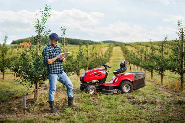 A serious mature farmer with tablet standing outdoors in orchard.