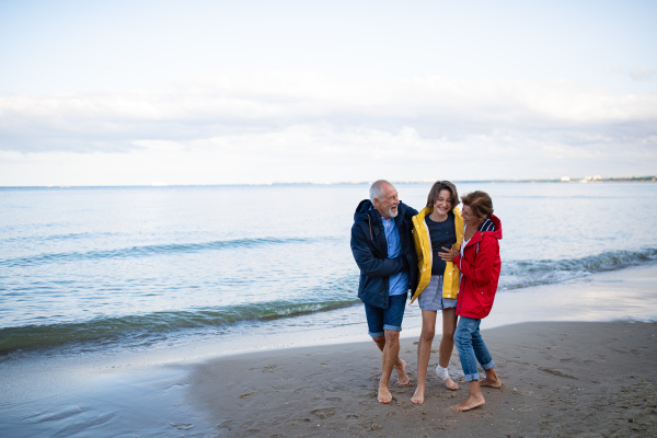 A senior couple and their preteen granddaughter hugging when walking on sandy beach.