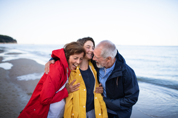 A senior couple and their preteen granddaughter hugging when walking on sandy beach.