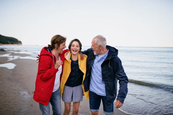 A senior couple and their preteen granddaughter hugging when walking on sandy beach.