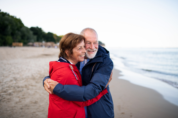 A happy senior couple in love embracing when walking on sandy beach in autumn.