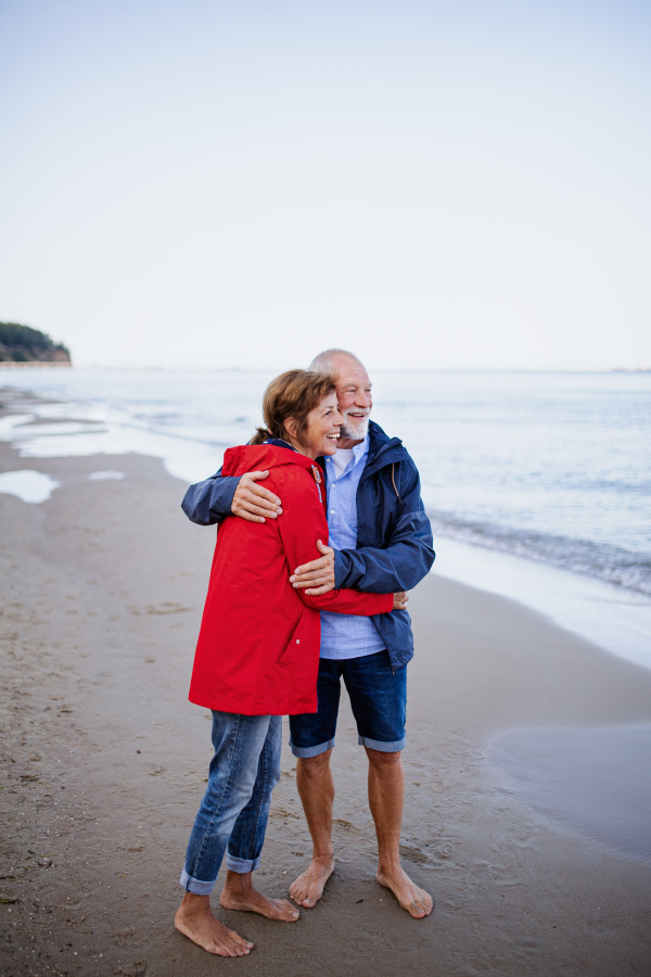 A happy senior couple in love embracing when walking on sandy beach.