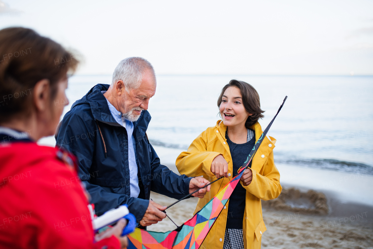 Grandparents with a preteen girl preparing kite for flying on sandy beach.