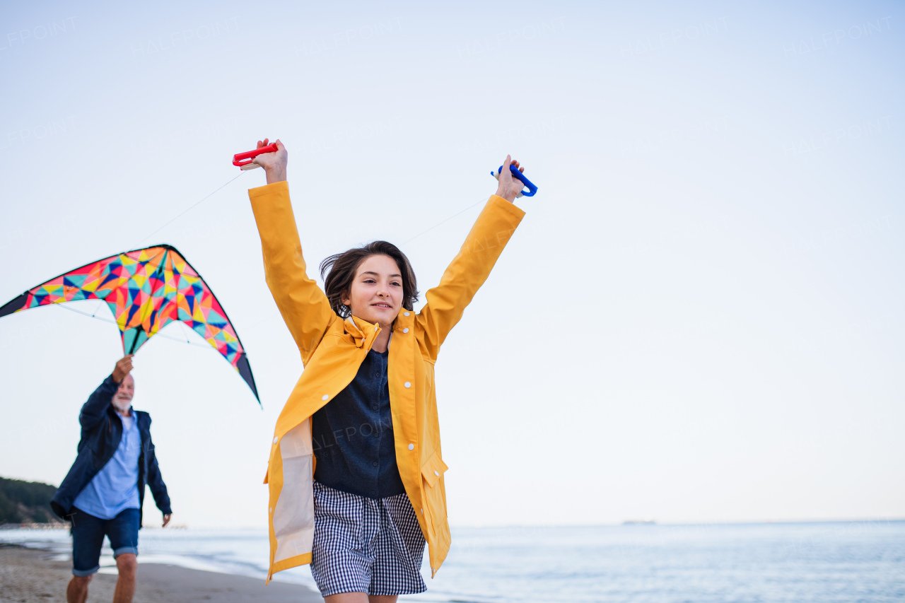 A low angle view of preteen girl and her grandfather playing with kite on sandy beach.