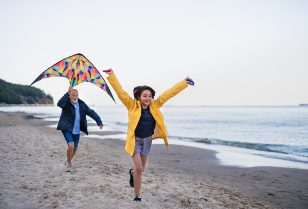 A senior man and his preteen granddaughter playing with kite on sandy beach.