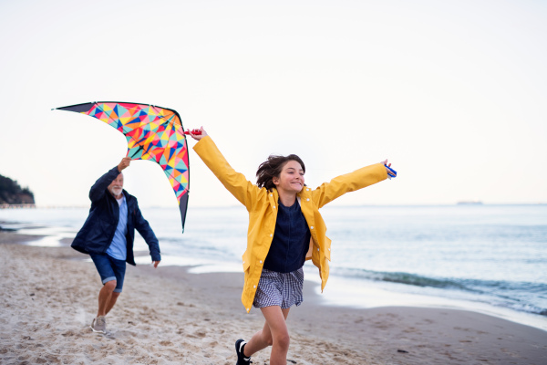 A senior man and his preteen granddaughter playing with kite on sandy beach.