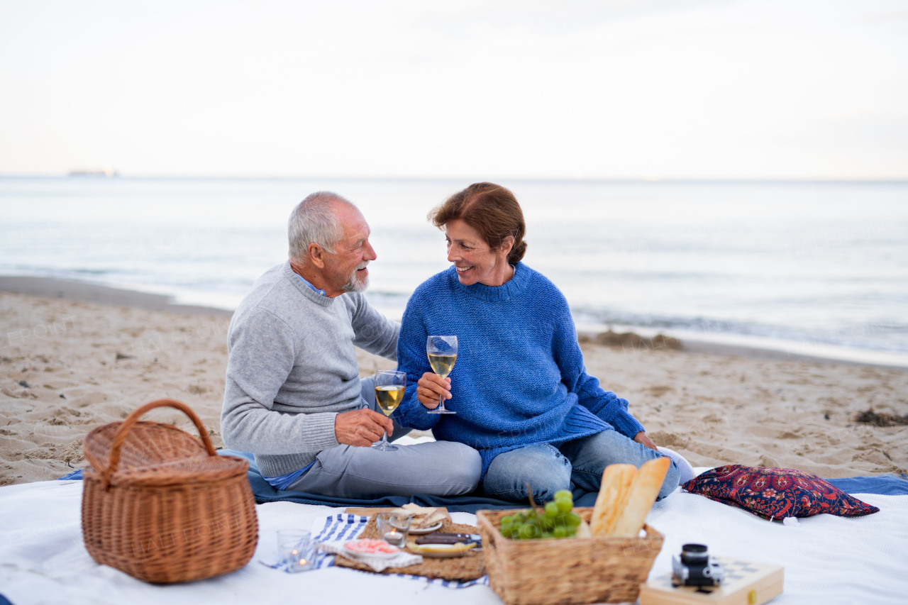 A happy senior couple in love sitting on blanket and embracing when having picnic outdoors on beach