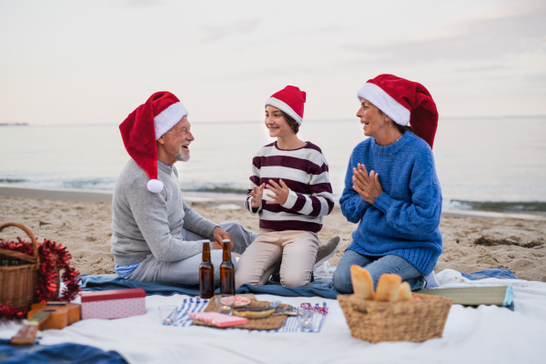 A senior couple with granddaugter celebrate New Year or Christmas and have picnic on beach.