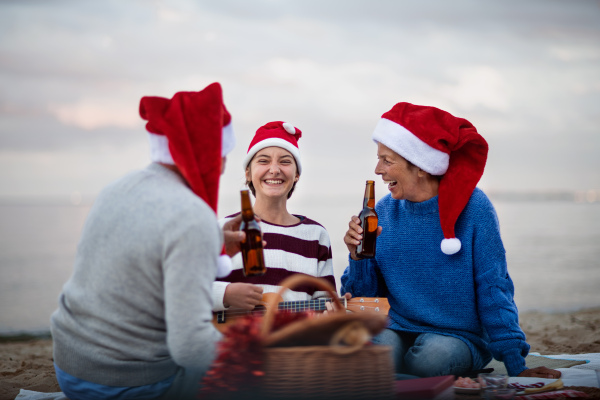 A senior couple with granddaugter with guitar celebrate New Year or Christmas and have picnic on beach.