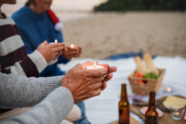 A close up of unrecognizable people celebrate Christmas and holding candles on beach.