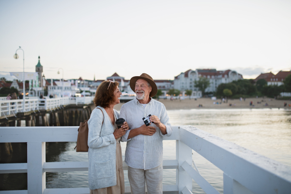 A happy senior couple tourist having fun on walk outdoors on pier by sea, summer holiday.