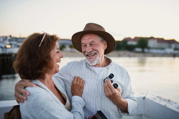 Happy senior couple in love hugging outdoors on pier by sea, looking at each otherand laughing.