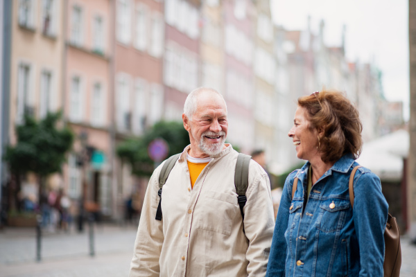 A portrait of happy senior couple tourists using smartphone outdoors in historic town