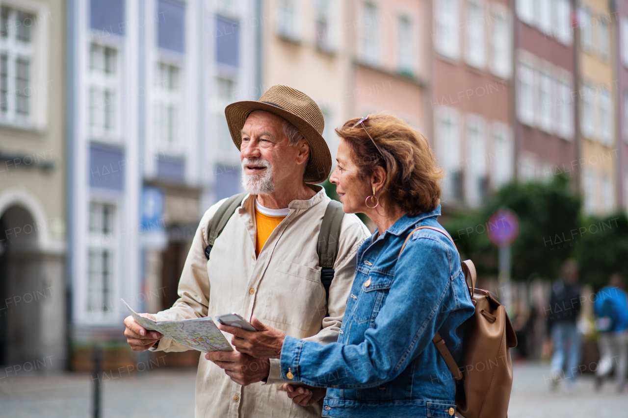 A portrait of happy senior couple tourists using map and smartphone outdoors in town street