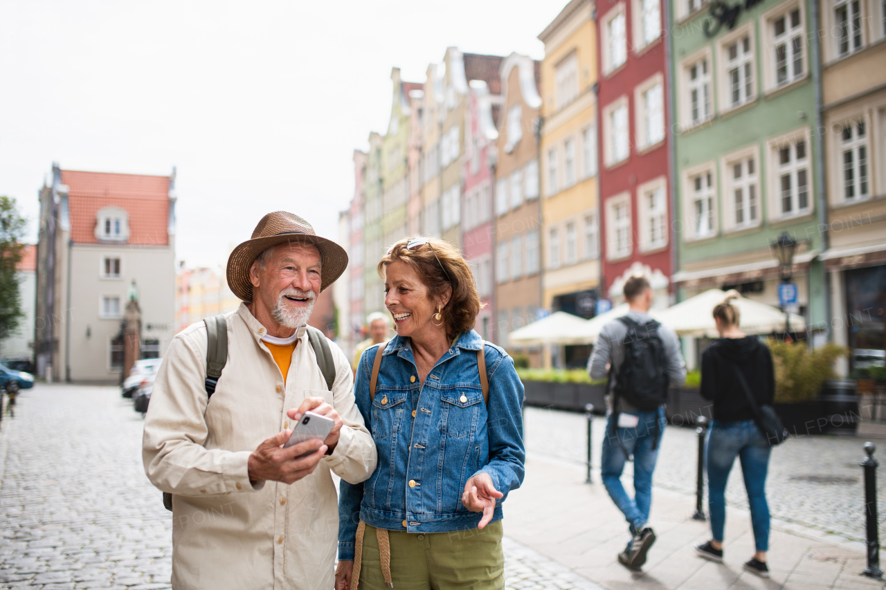 A portrait of happy senior couple tourists using smartphone outdoors in historic town