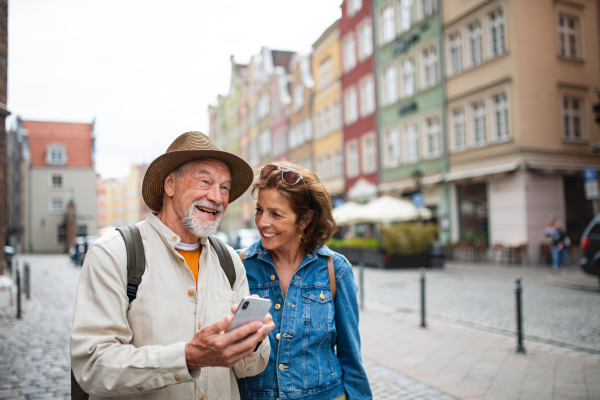 A portrait of happy senior couple tourists using smartphone outdoors in historic town