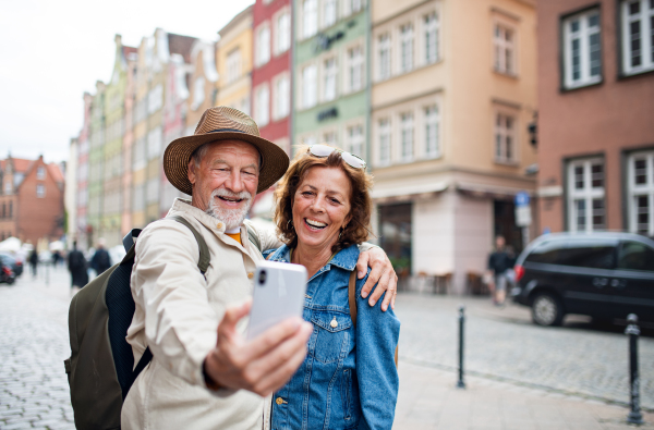 A portrait of happy senior couple tourists doing selfie outdoors in historic town