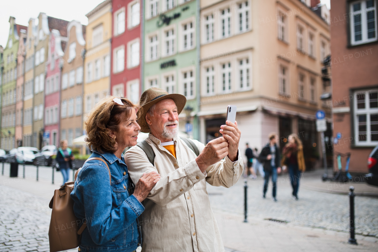 A portrait of happy senior couple tourists doing selfie outdoors in historic town