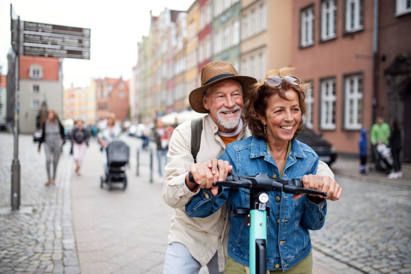 A portrait of happy senior couple tourists riding scooter together outdoors in town