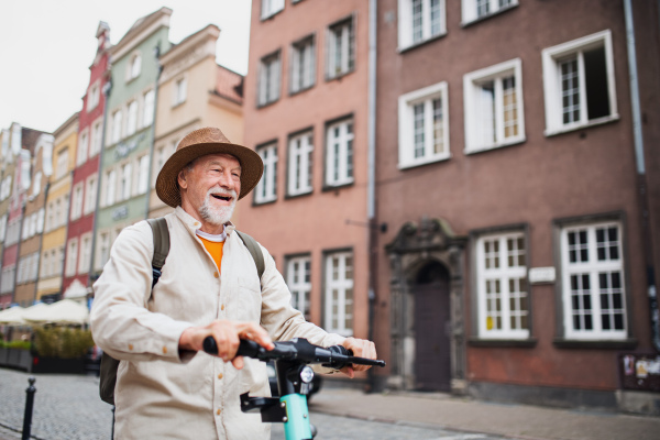 A portrait of happy senior man tourist riding scooter outdoors in town