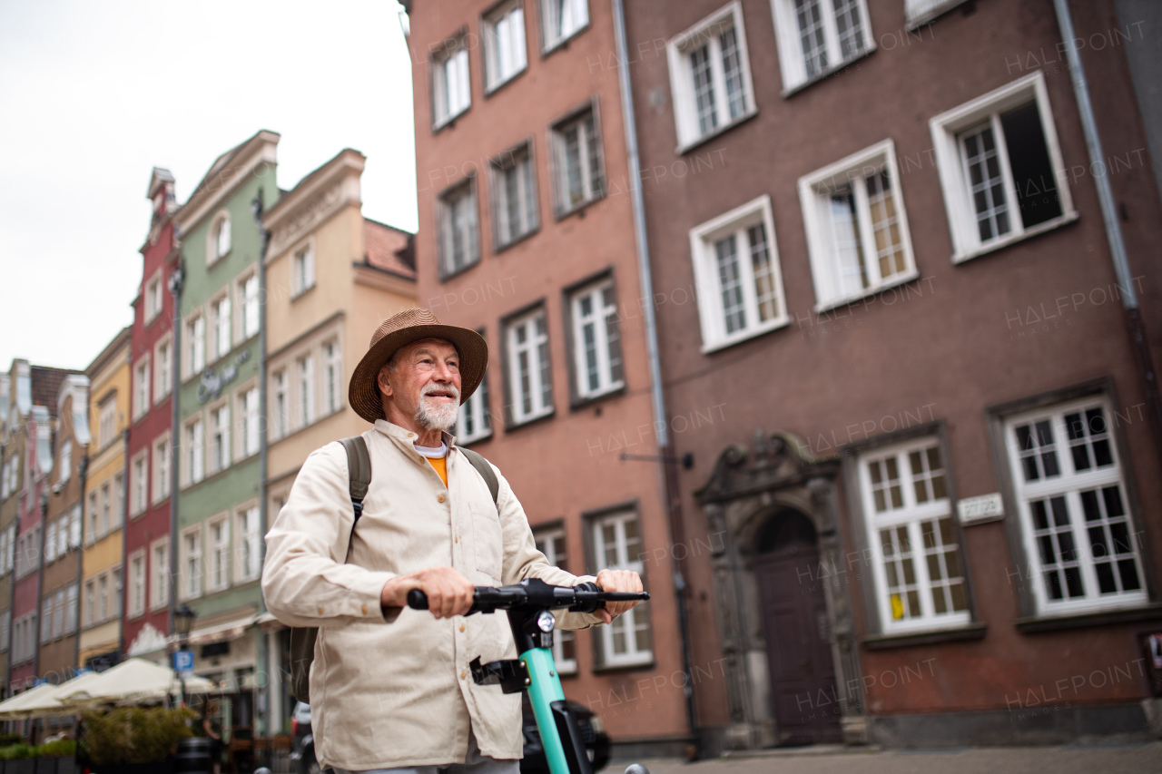 A portrait of happy senior man tourist riding scooter outdoors in town