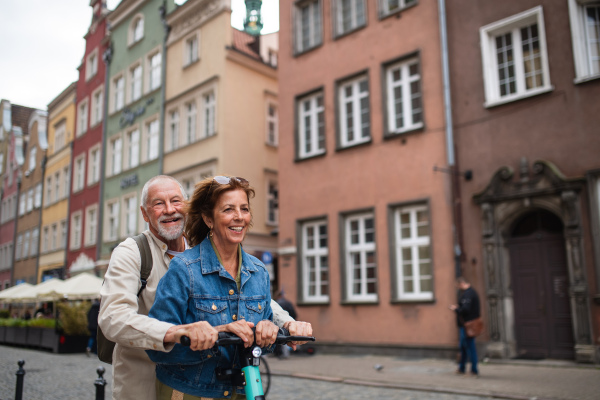 A portrait of happy senior couple tourists riding scooter together outdoors in town