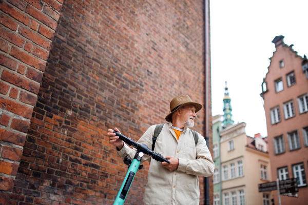 A portrait of happy senior man tourist riding scooter outdoors in town