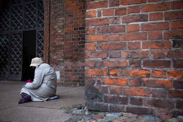 A homeless beggar man sitting outdoors in city asking for money donation.