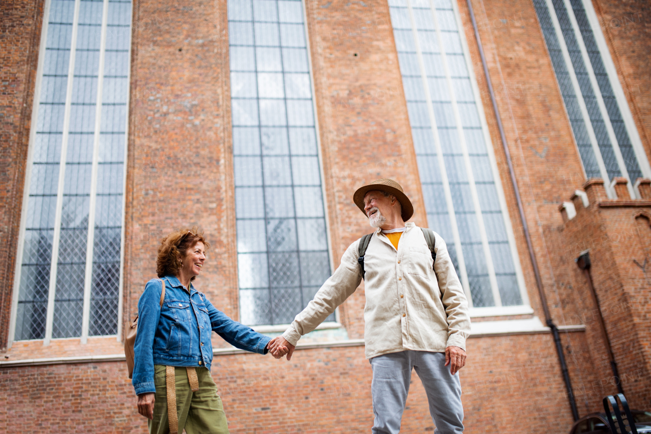 A low angle view of happy senior couple in love holding hands outdoors in town