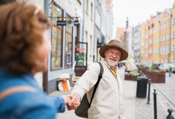 A happy senior woman giving hand to senior man, couple in love holding outdoors in town