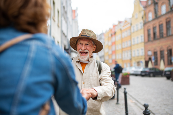 A happy senior man giving hand to senior woman, couple in love holding outdoors in town