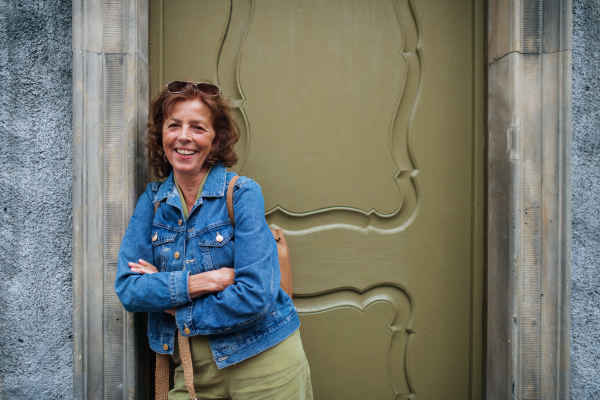 A happy senior woman tourist posing next to historic building's door in town