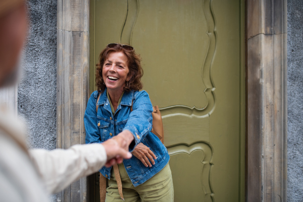 A happy senior woman giving hand to senior man, couple in love holding outdoors in town