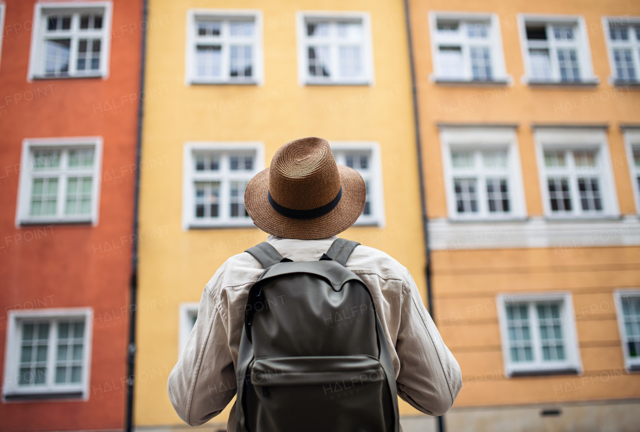 A rear view of senior man tourist outdoors looking at apartment building