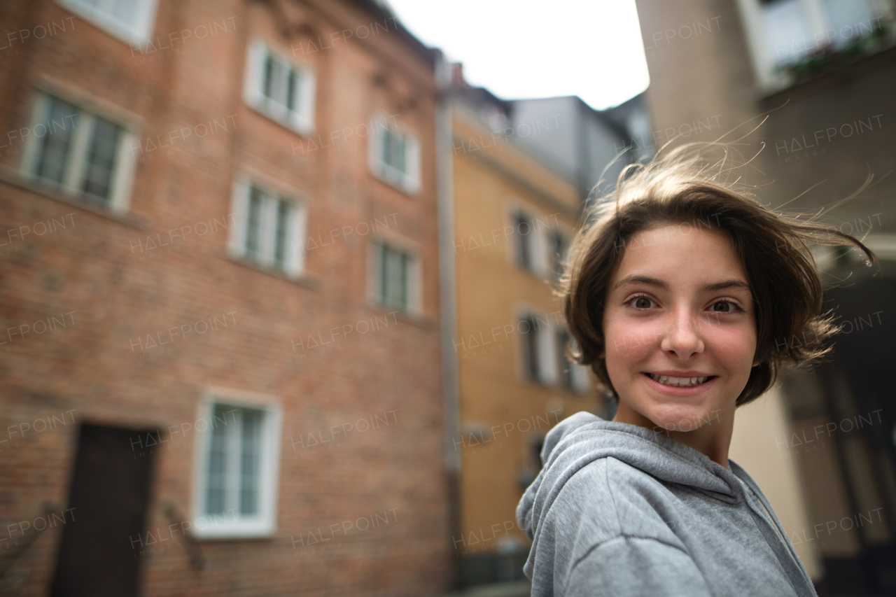 A portrait of happy preteen girl turning round and looking at camera outdoors in street.