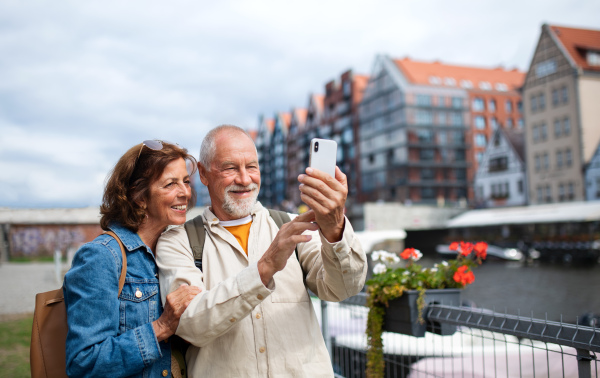 A portrait of happy senior couple tourists doing selfie outdoors in historic town