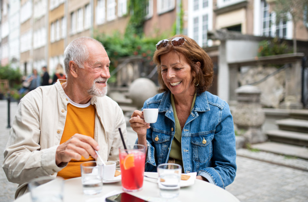 A portrait of happy senior couple sitting and having coffee outdoors in cafe.