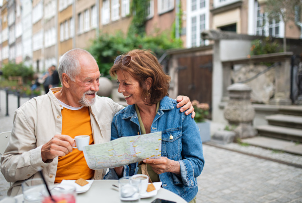 A portrait of happy senior couple tourists sitting and using map outdoors in town.