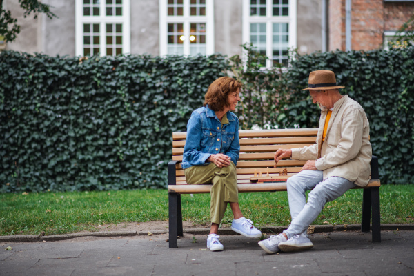 A happy senior couple sitting on bench and playing chess outdoors in park.