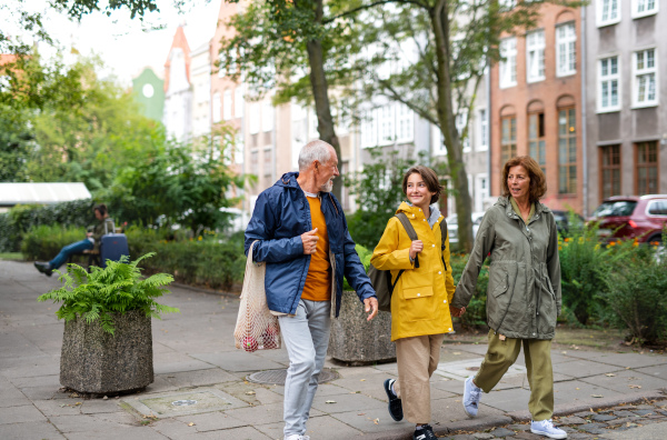 A portrait of happy grandparents with preteen grandddaughter walking together ourtdoors in town street