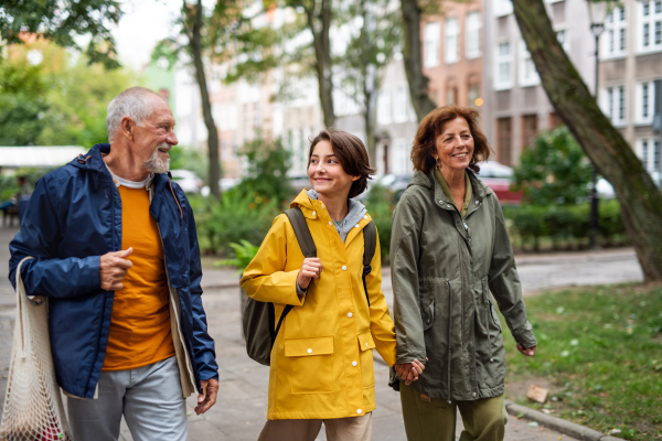 A portrait of happy grandparents with preteen grandddaughter walking together ourtdoors in town street