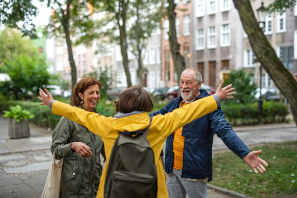 Happy grandparents with a preteen grandddaughter hugging together ourtdoors in town street