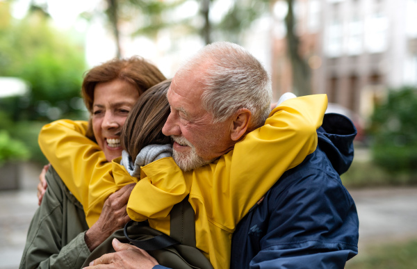 Happy grandparents with a preteen grandddaughter hugging together ourtdoors in town street