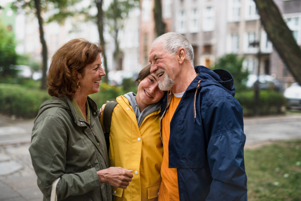 Happy grandparents with a preteen grandddaughter hugging together ourtdoors in town street