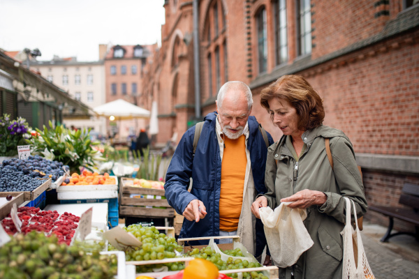 A happy senior couple tourists buying fruit outdoors on market in town.