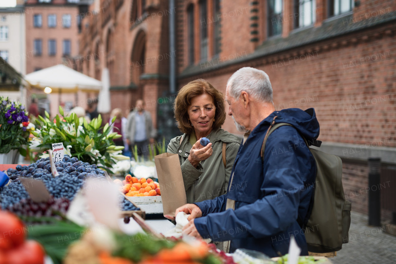 A happy senior couple tourists buying fruit outdoors on market in town.