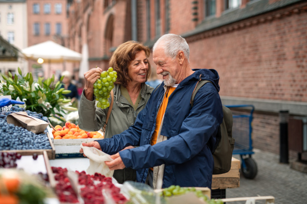 A happy senior couple tourists buying fruit outdoors on market in town.