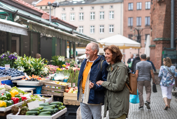 A happy senior couple tourists buying fruit outdoors on market in town.