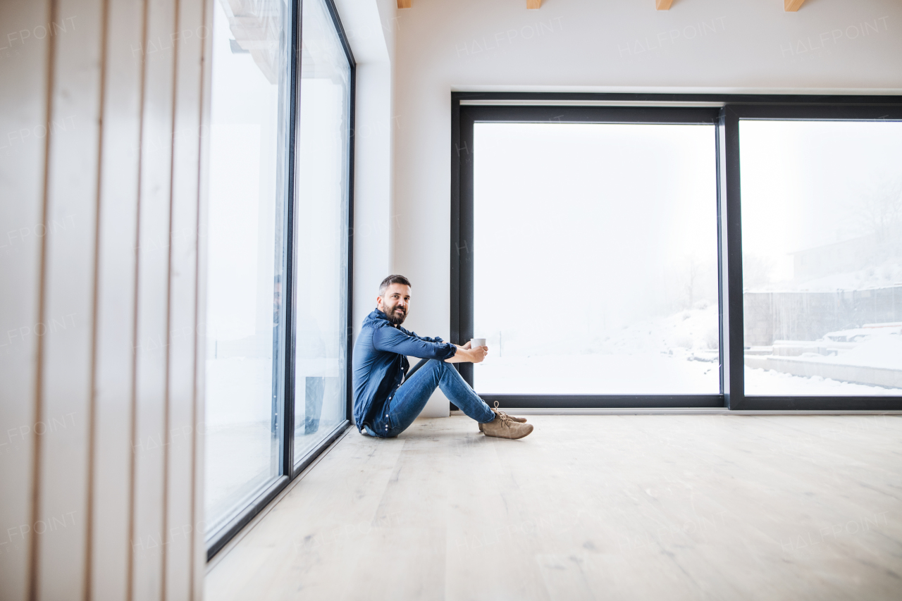 A mature man sitting on the floor in unfurnished new house, holding coffee. A new home concept. Copy space.